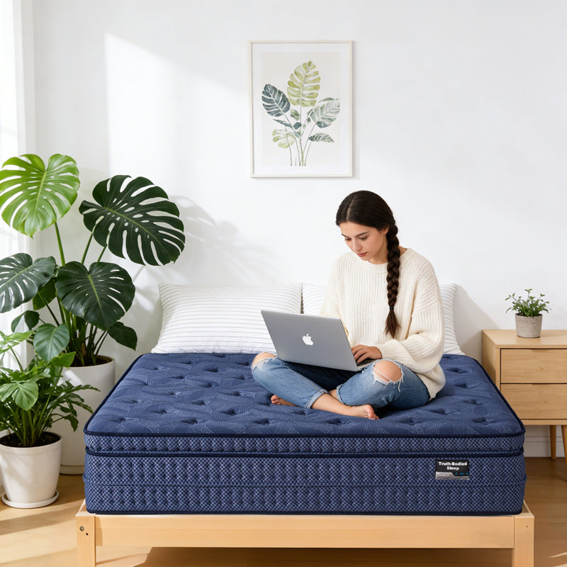 Woman using a laptop on a suiforlun blue mattress in a room with plants and a plant on a nightstand.