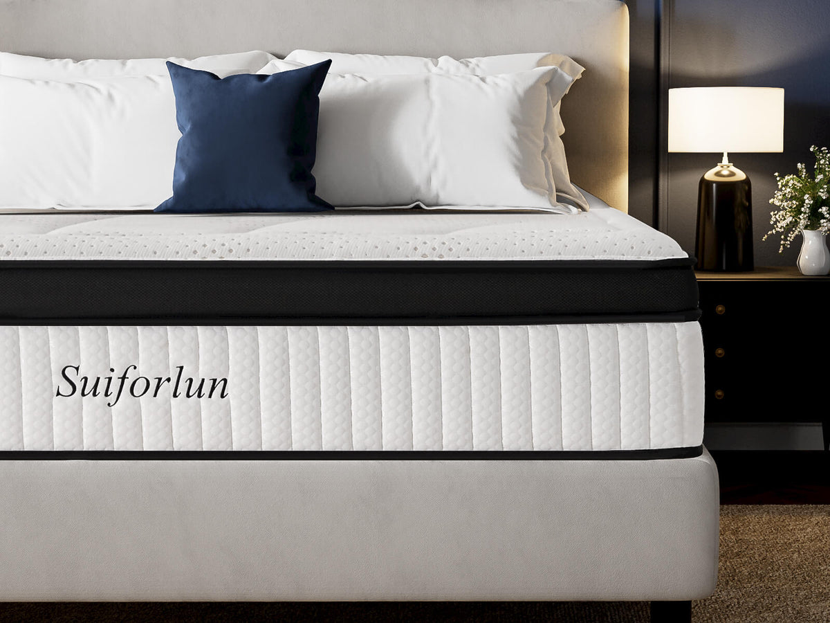 A bed with a white quilted mattress featuring black trim and the brand name 'Suiforlun' printed on the side, styled with white and navy blue pillows in a modern bedroom setting.