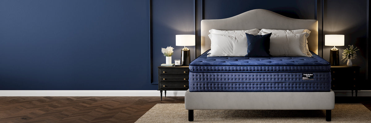 A luxury bed with a deep blue quilted mattress and matching blue bedding, set in a modern bedroom with a gray upholstered headboard, dark wood nightstands, and a deep navy blue wall.